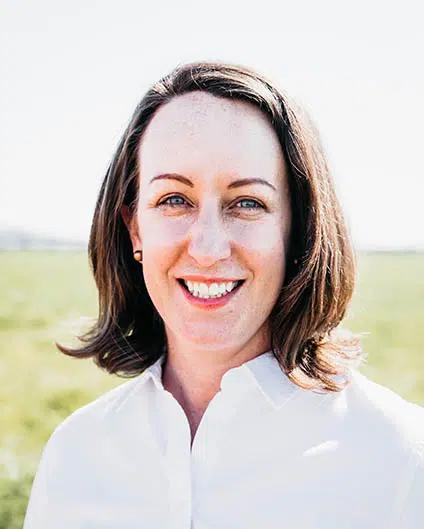 Carmen Quade agri business expert is standing in a green paddock she is wearing a white blouse.